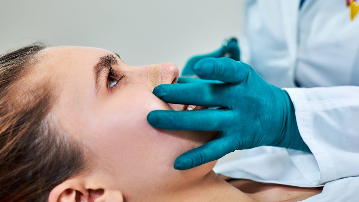 Young woman having her new nose examined at a follow-up appointment with her rhinoplasty surgeon 