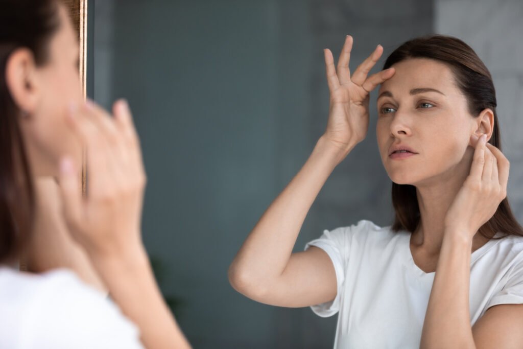 Woman frowning at her forehead in the mirror